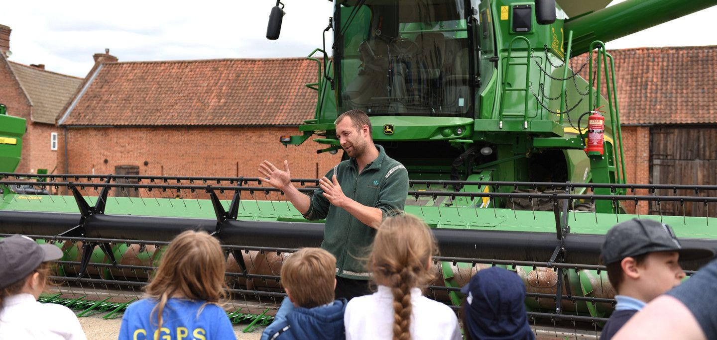 farmer standing infront of a combine harvester talking to children
