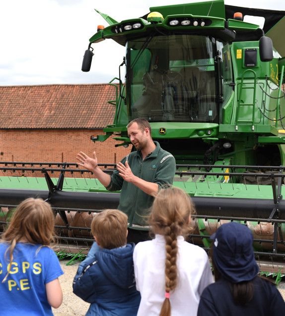farmer standing infront of a combine harvester talking to children