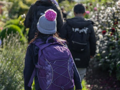 girl walks through walled garden wearing a coat and bobble hat
